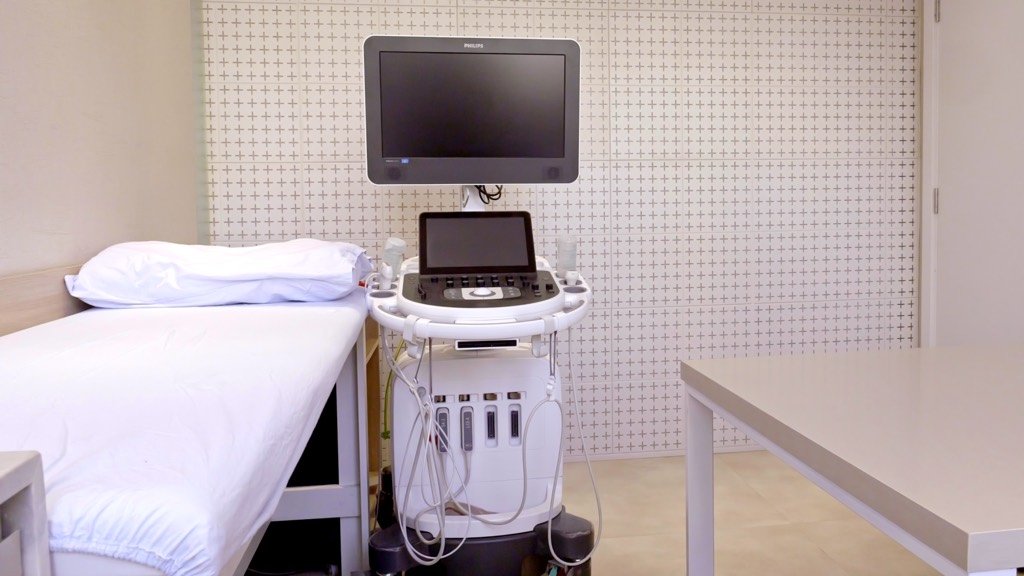 Sala de ecocardiograma com maca preparada e o aparelho de ultrassom ao lado.