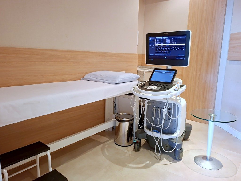 Aparelho de ecocardiografia com a imagem do coração na tela, ao lado da maca preparada.